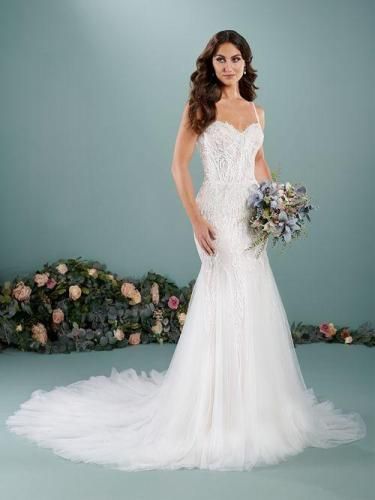 Woman in a white wedding dress holding flowers; light blue background, floral arrangement in front.
