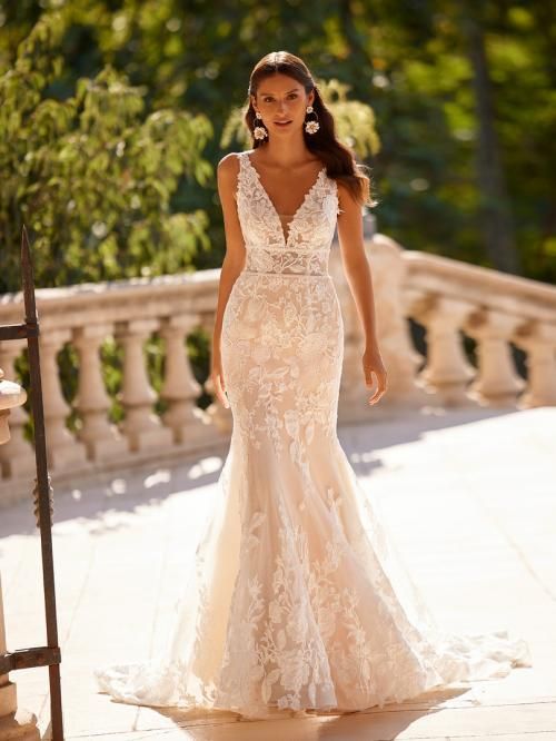 Woman in a lace mermaid wedding dress with a deep V-neck, standing on stone steps outdoors.