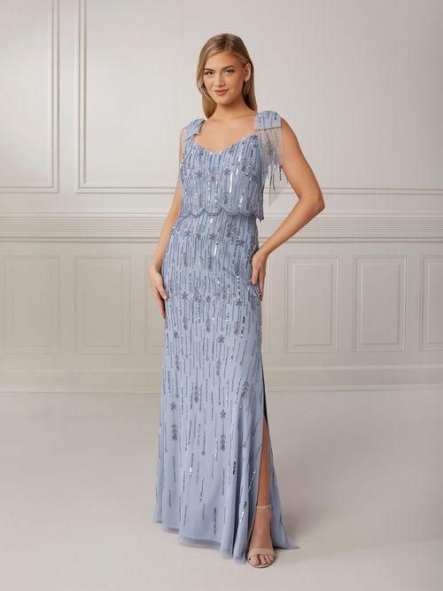 Woman in a light blue, beaded formal gown with a shoulder cape, standing in a bright room.