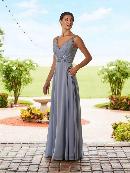 Woman in a blue dress with lace bodice, standing outdoors with a garden background.