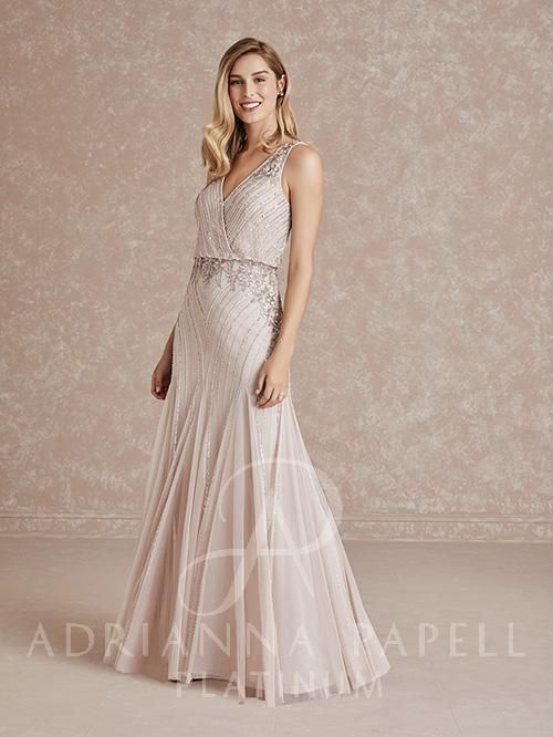 Woman in a beaded blush gown, posing in front of a patterned wall.