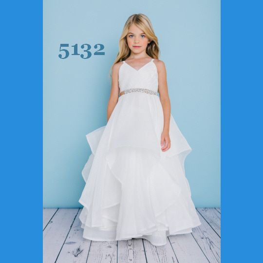 Girl in white formal dress with rhinestone belt stands in front of a blue wall.