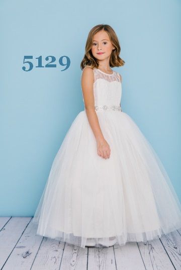 Girl in white formal dress, smiling, standing against blue backdrop, wooden floor, number 5129 visible.