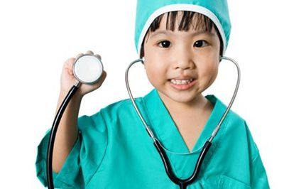 Child in green scrubs holding a stethoscope and smiling at the camera