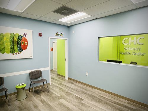 Bright waiting room with blue walls, lime-green accents, chairs, and a reception window labeled GHC Pediatrics & Family Medicine