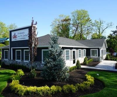 Small gray office building with white trim, landscaped shrubs, and a sign at the front entrance