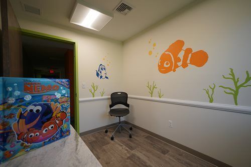 Small decorated room with a chair, toy box, and orange fish wall mural under bright ceiling lights