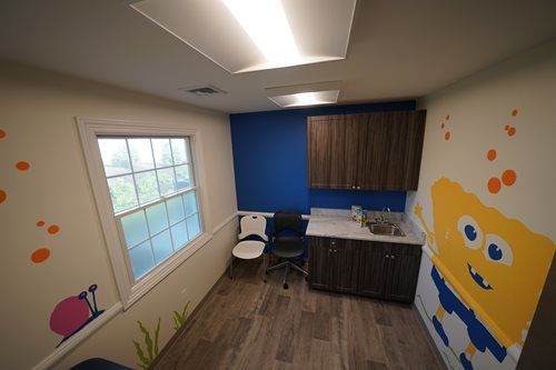 Small colorful room with desk, chair, window, blue accent wall, and cartoon mural on the right side.