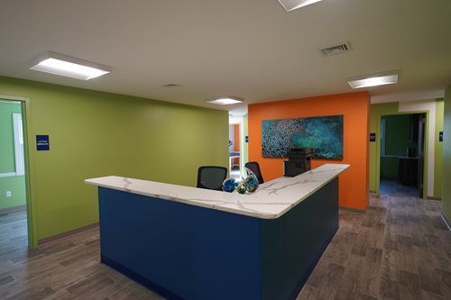 Modern office lobby with green walls, blue reception desk, and orange accent wall