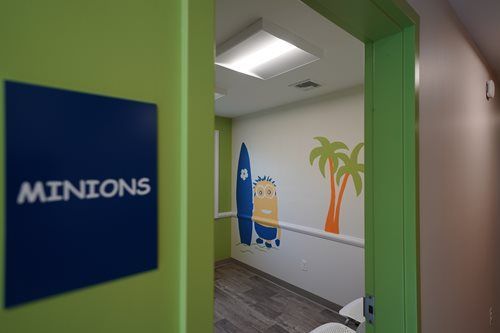 Minions-themed hallway with green doorway, blue sign, and wall mural of a Minion and palm trees