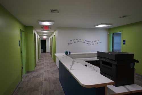 Empty office hallway with lime-green walls, carpeted floor, and a reception desk on the right.