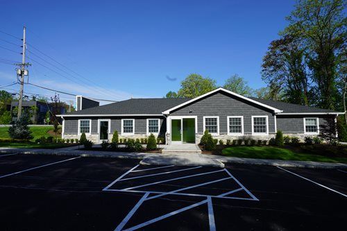 Single-story white building with dark roof and parking lot in front under a clear blue sky