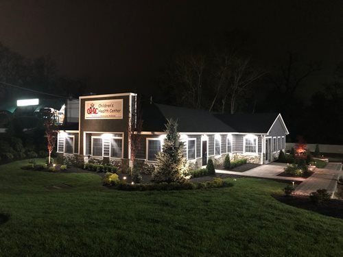 Nighttime view of a lit restaurant building with a sign, lawn, and parked cars.