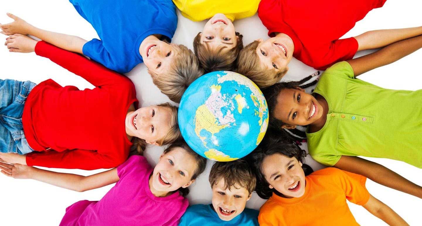 Children in colorful shirts lie in a circle around a globe, smiling up at the camera.