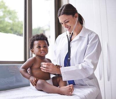 Doctor using a stethoscope to examine a baby on an exam table by a window