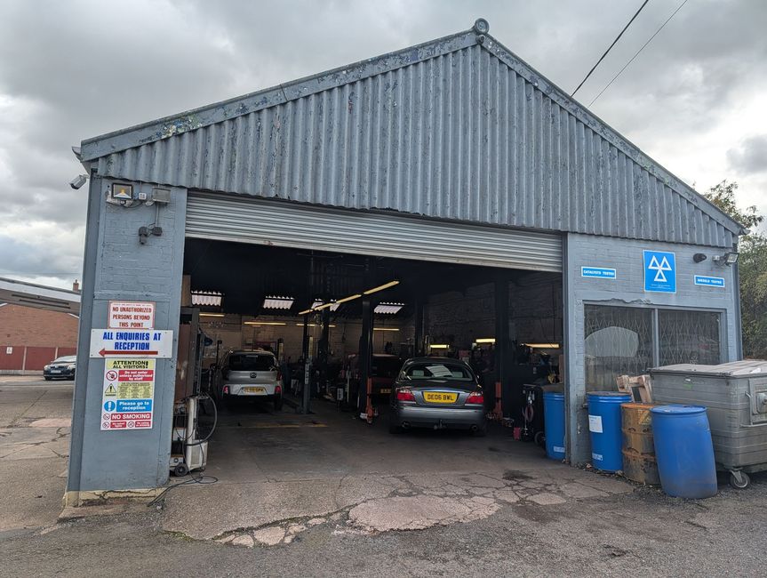 Auto repair garage with open bays, cars inside, and blue bins outside under a gray sky