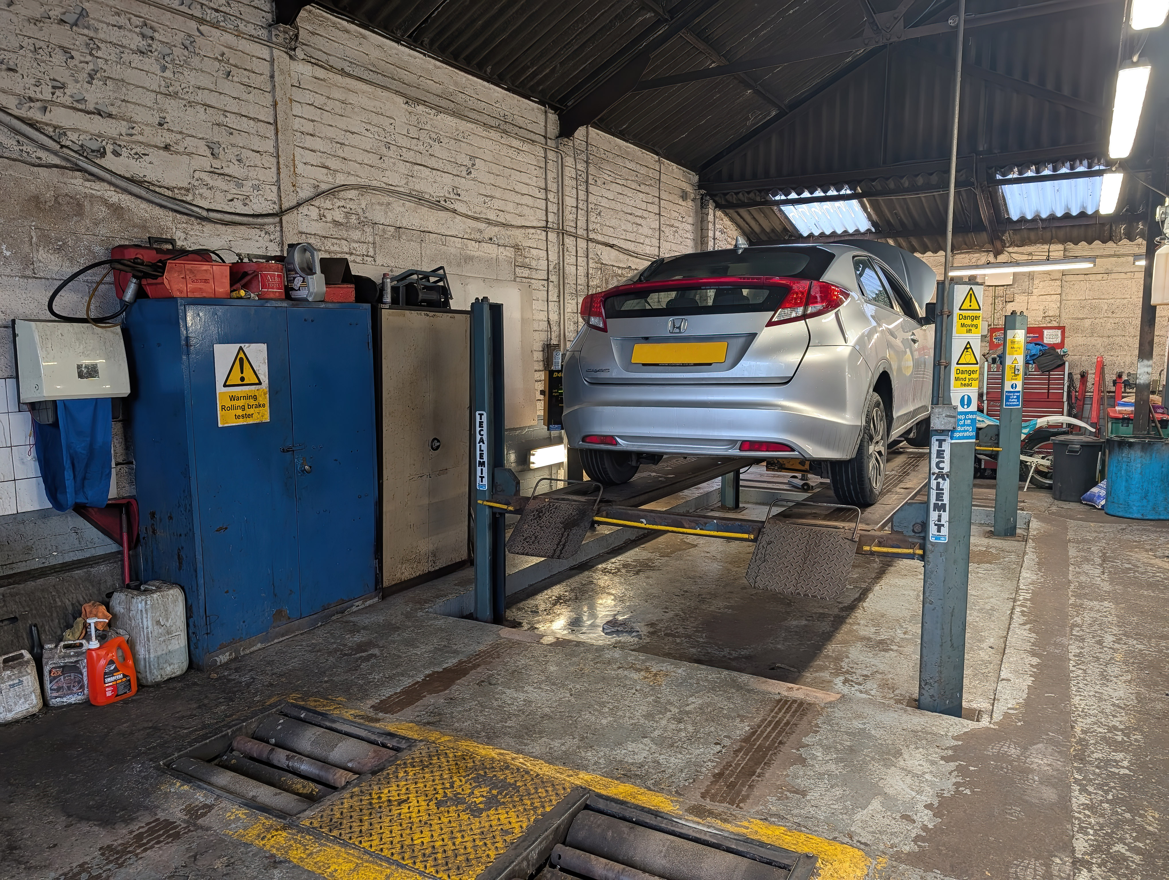 Silver car lifted on a blue hydraulic lift in an auto repair garage with tools and equipment nearby