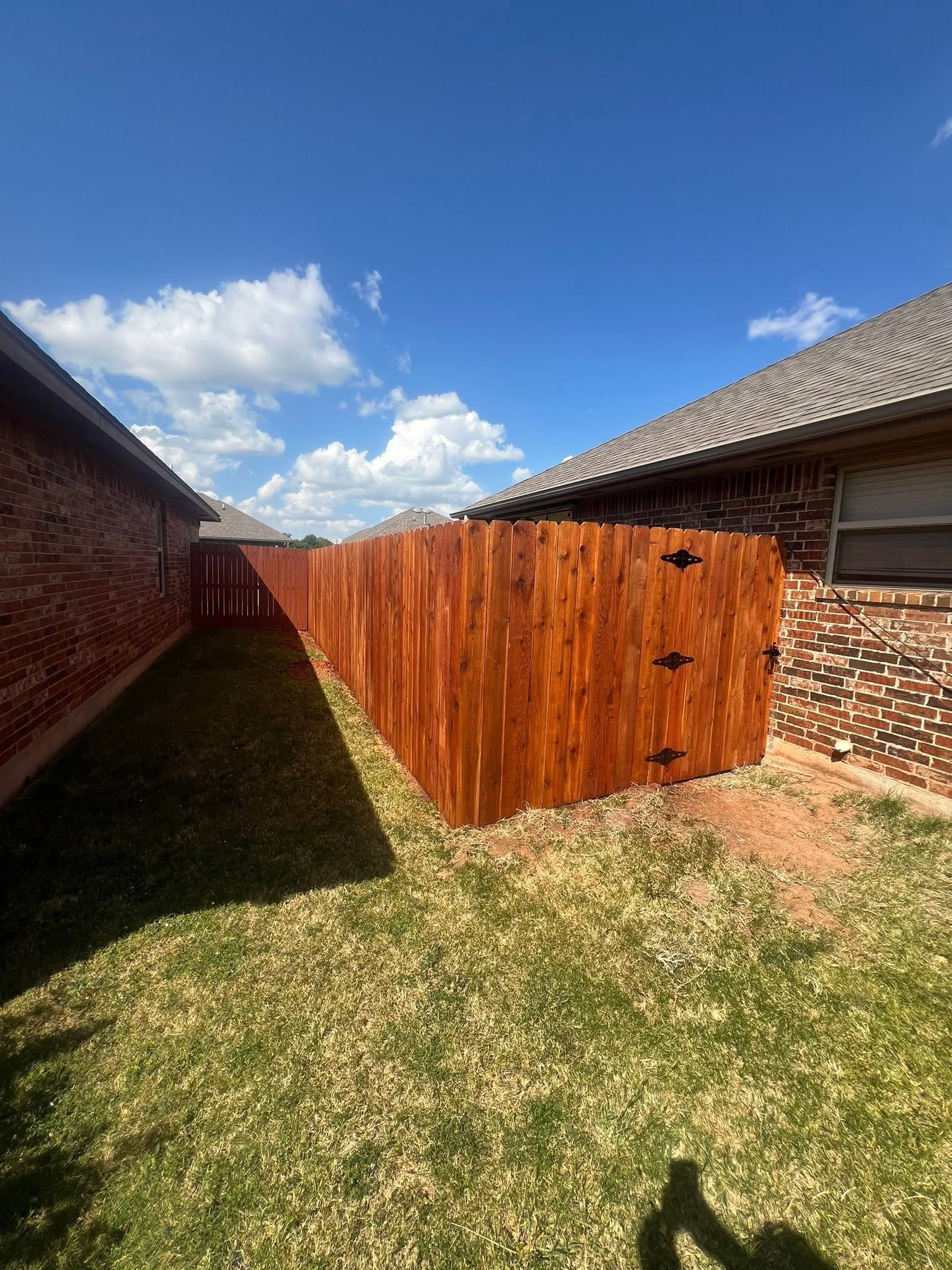 Backyard between brick houses with a wooden privacy fence and a blue sky with clouds