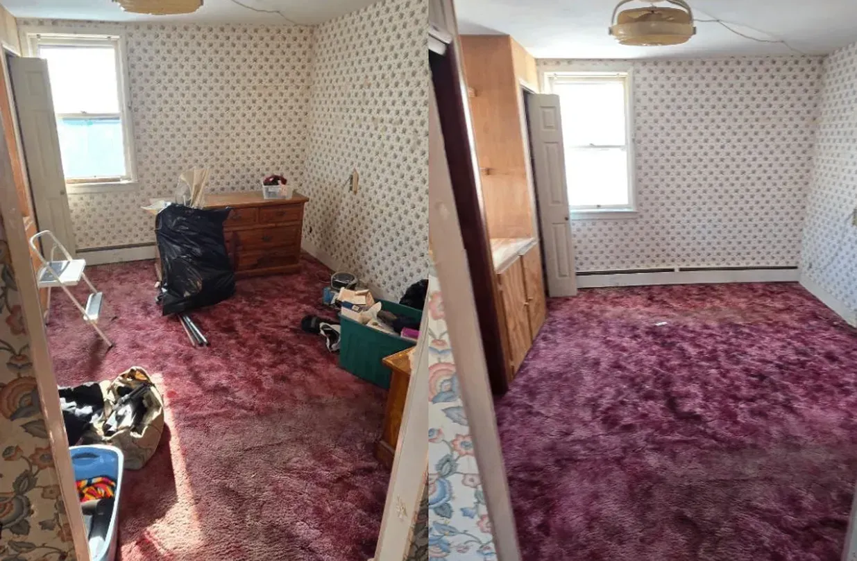 Small carpeted room with patterned wallpaper, a dresser, and boxes near two windows.