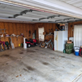 Garage with wood-paneled walls, concrete floor, stored bikes, lawn tools, a red mower, and a white refrigerator