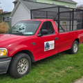 Red pickup truck with a black cargo cage parked on grass beside a house.