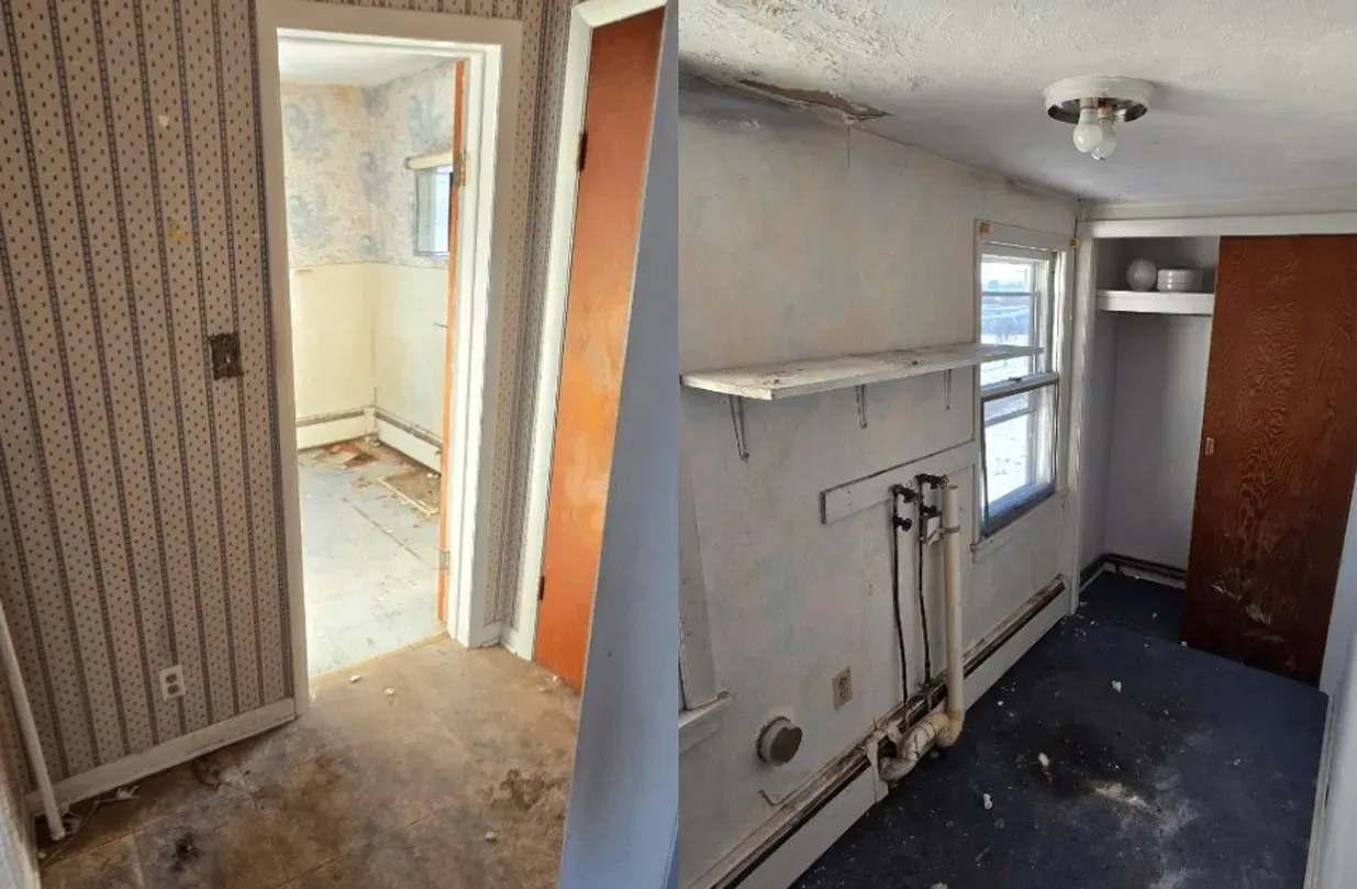 Old, narrow interior room with striped wallpaper, a doorway, window, shelf, and exposed plumbing by a dark floor
