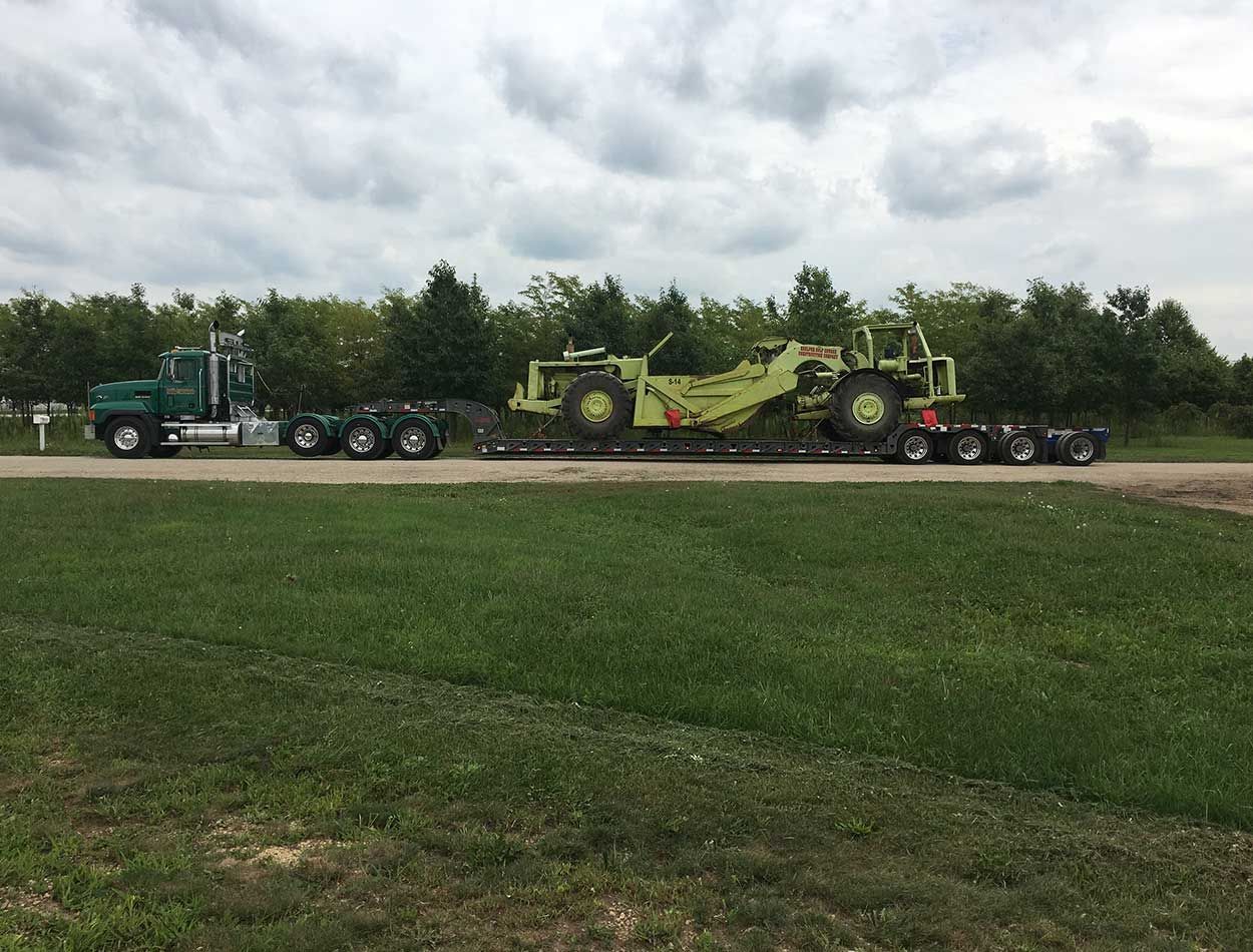 Green combine harvester on a lowboy trailer being hauled along a road under cloudy skies