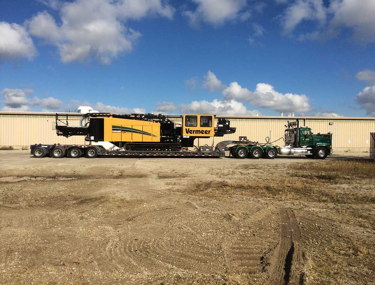 Yellow and black industrial machine on a trailer in a dirt lot under a blue sky