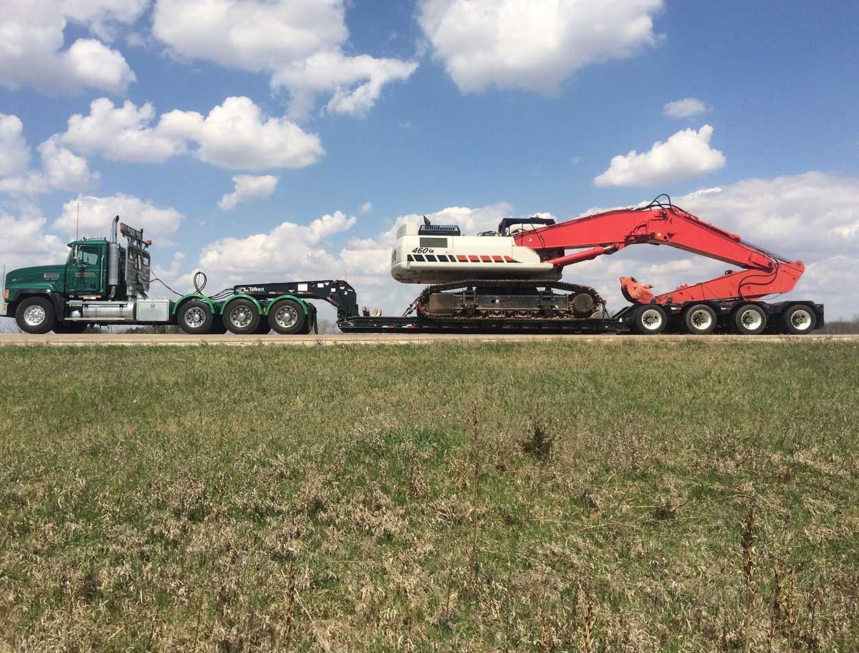 Tractor hauling a large farming machine across a field under a blue sky with clouds