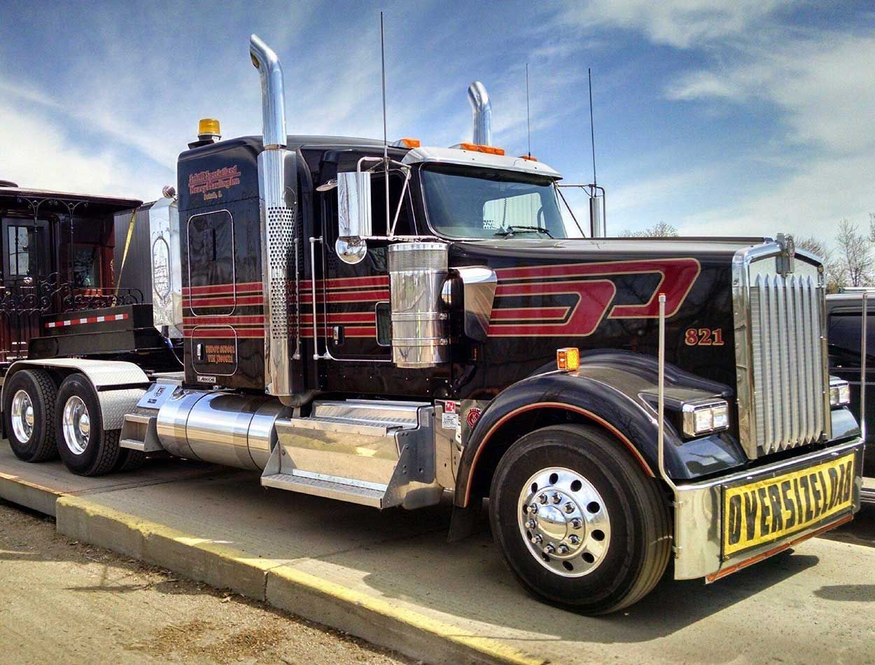 Black semi-truck with chrome details parked on a street under a blue sky