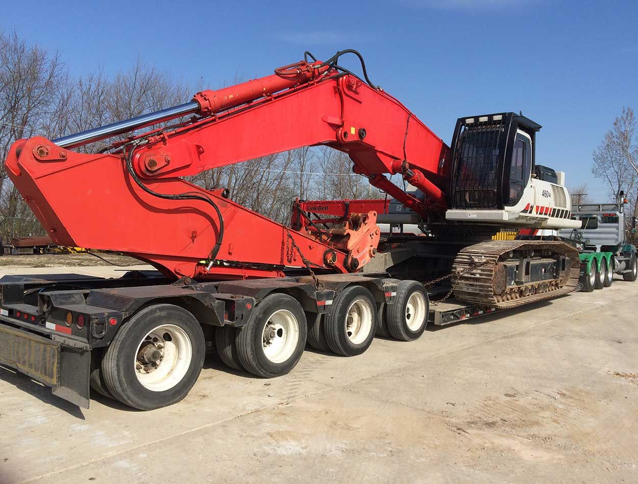 Red excavator loaded on a flatbed trailer in an outdoor construction yard