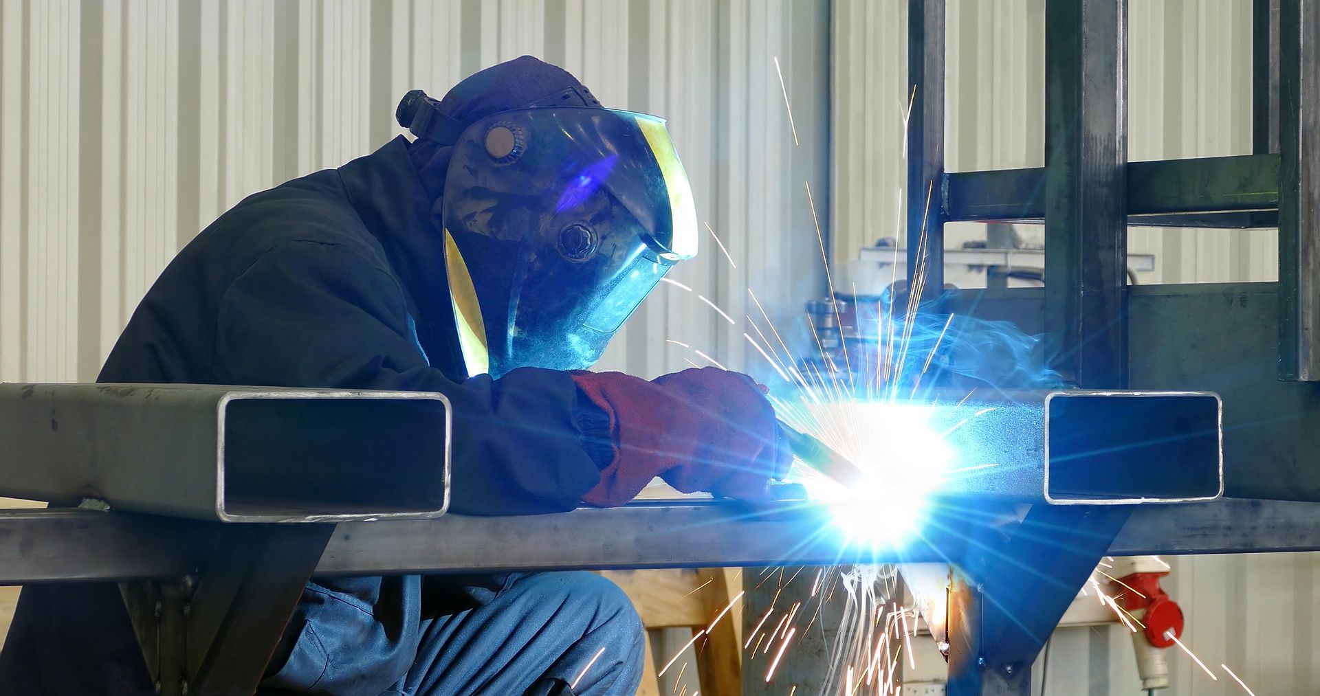 Welder in protective gear welding bright blue sparks on a metal frame indoors