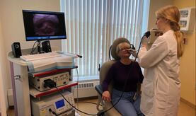 A woman is sitting in a chair while a doctor examines her throat.