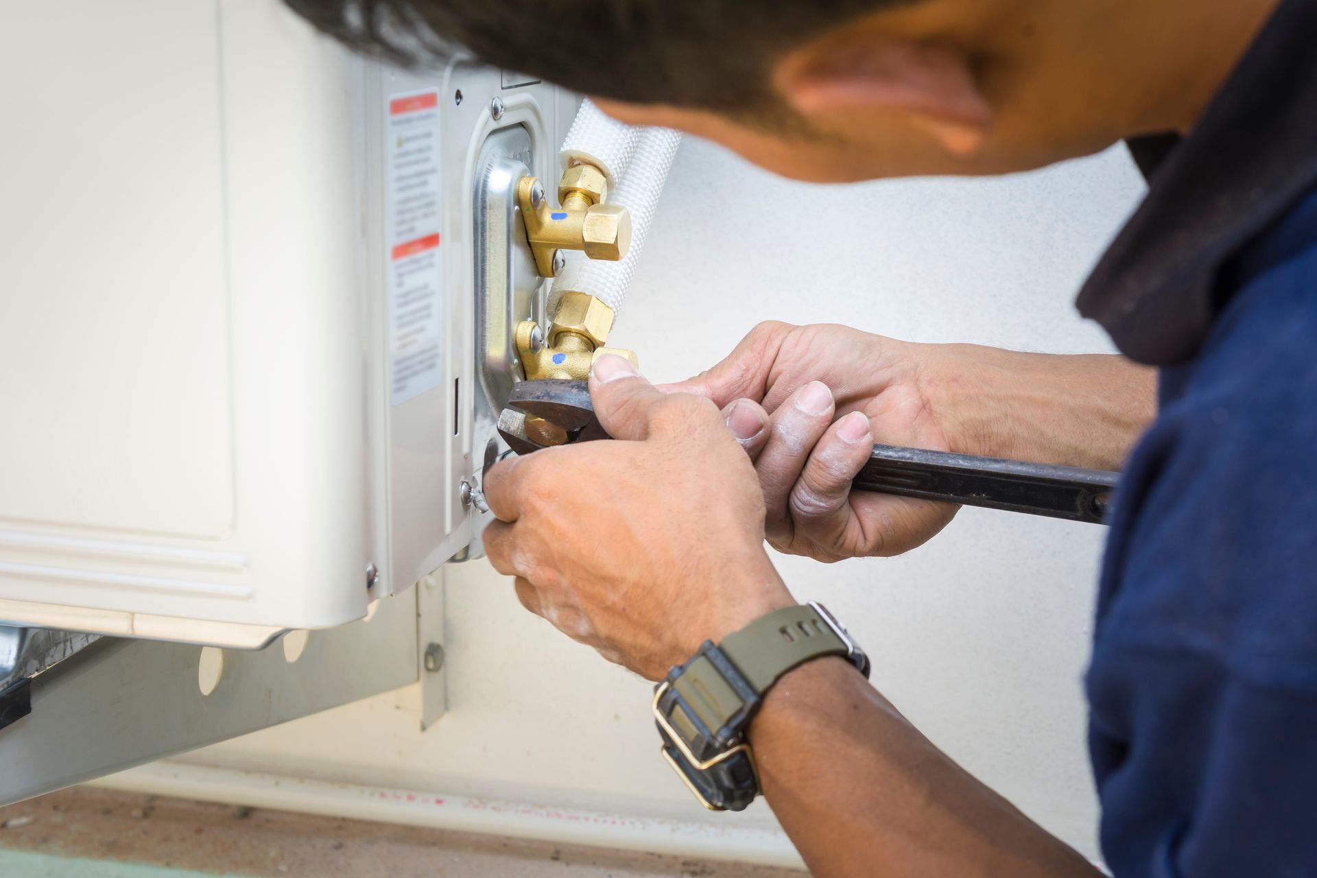 A man is fixing an air conditioner with a wrench.