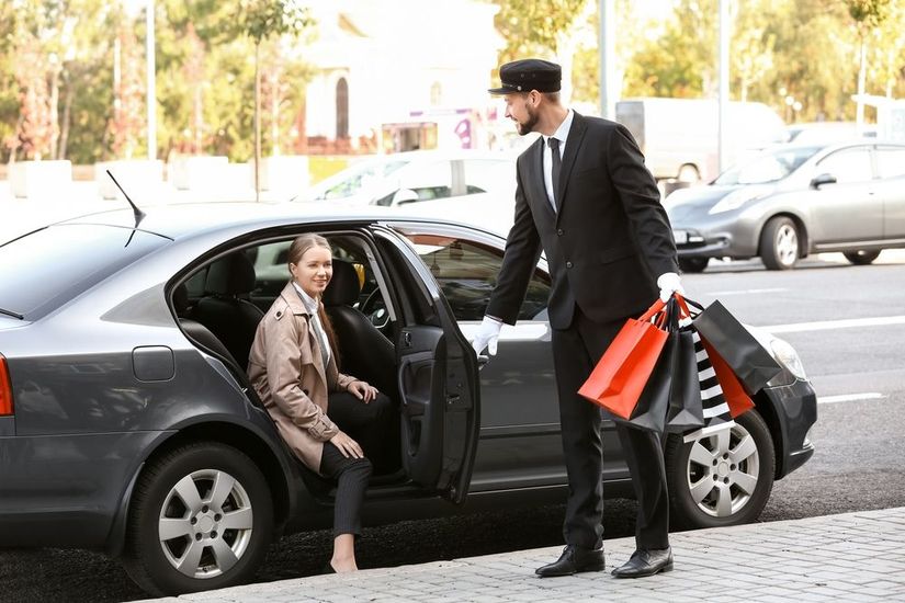 Butler in black suit opening car door for passenger with red carpet.