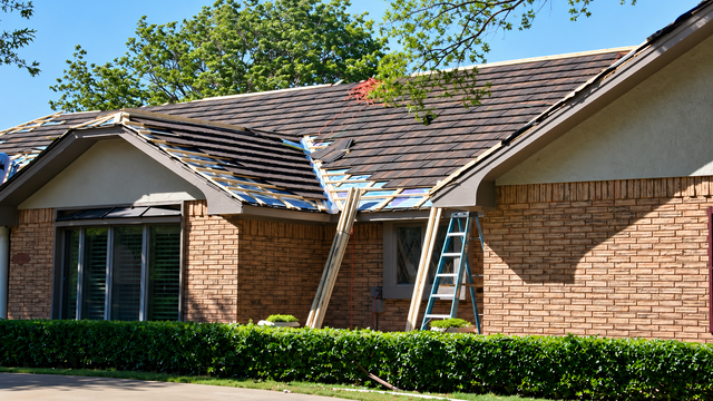 Brick house roof with ladder and exposed repair area under blue sky