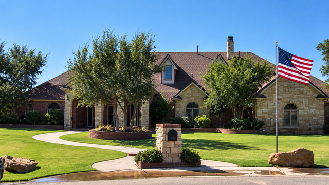 Stone house with front lawn, curved walkway, and American flag on a bright day