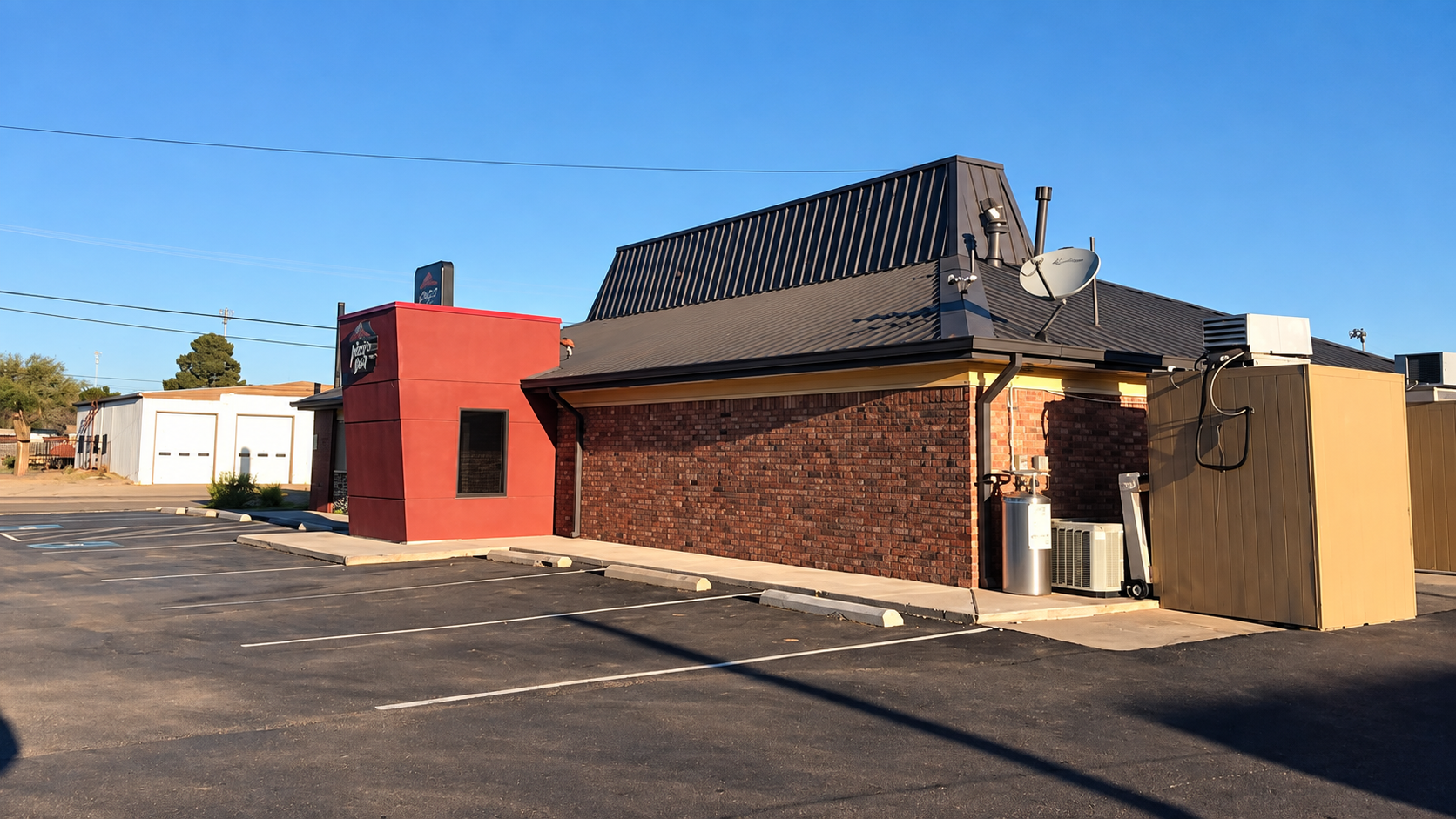Street view of a small brick building with a black tiled roof, red side wall, and parking lot in front