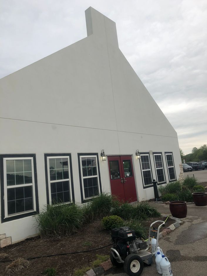 White house with black-trimmed windows, red door, potted plants, and a scooter outside under a cloudy sky.
