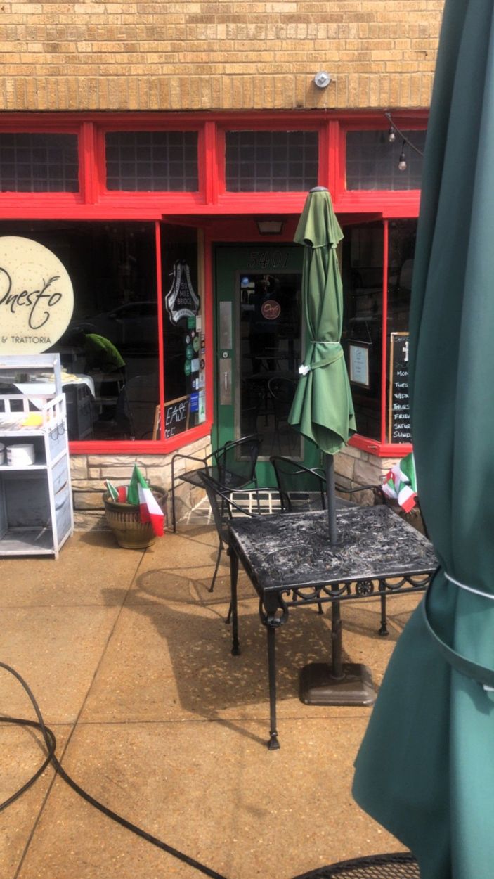 Outdoor café patio with red storefront windows, green umbrella, metal table, and wet pavement.