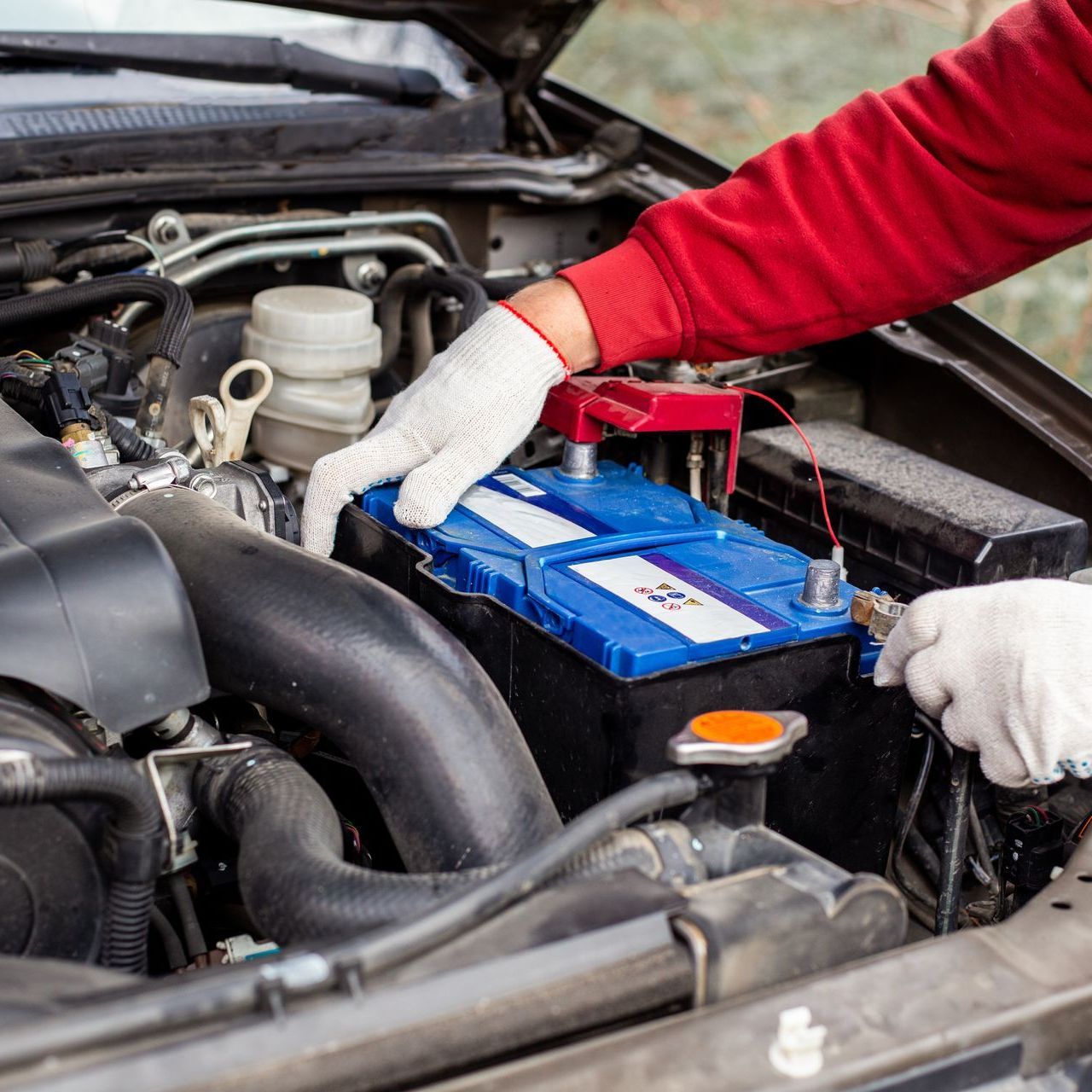 A person is working on a car battery with the hood open