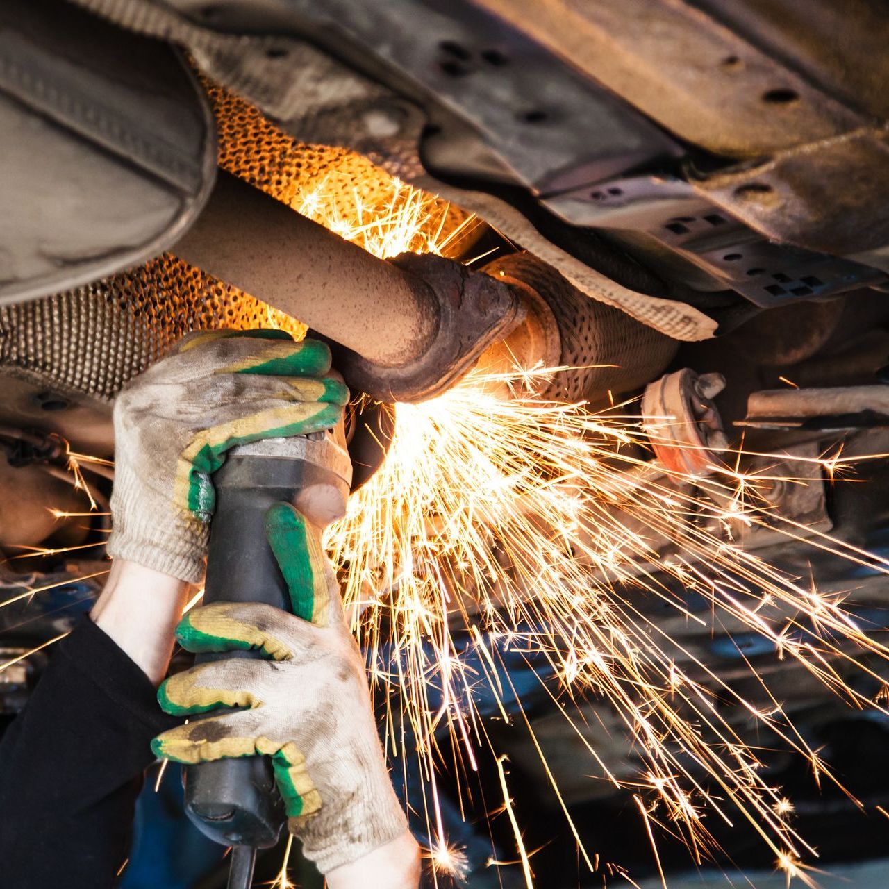 A man wearing green gloves is grinding a exhaust pipe on a car