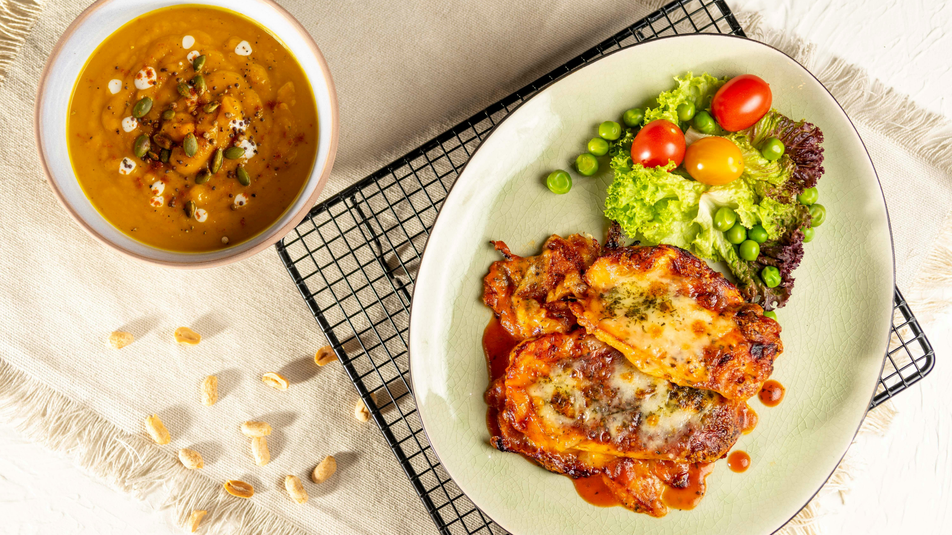 Soup and a plate of food with salad, on a white surface.
