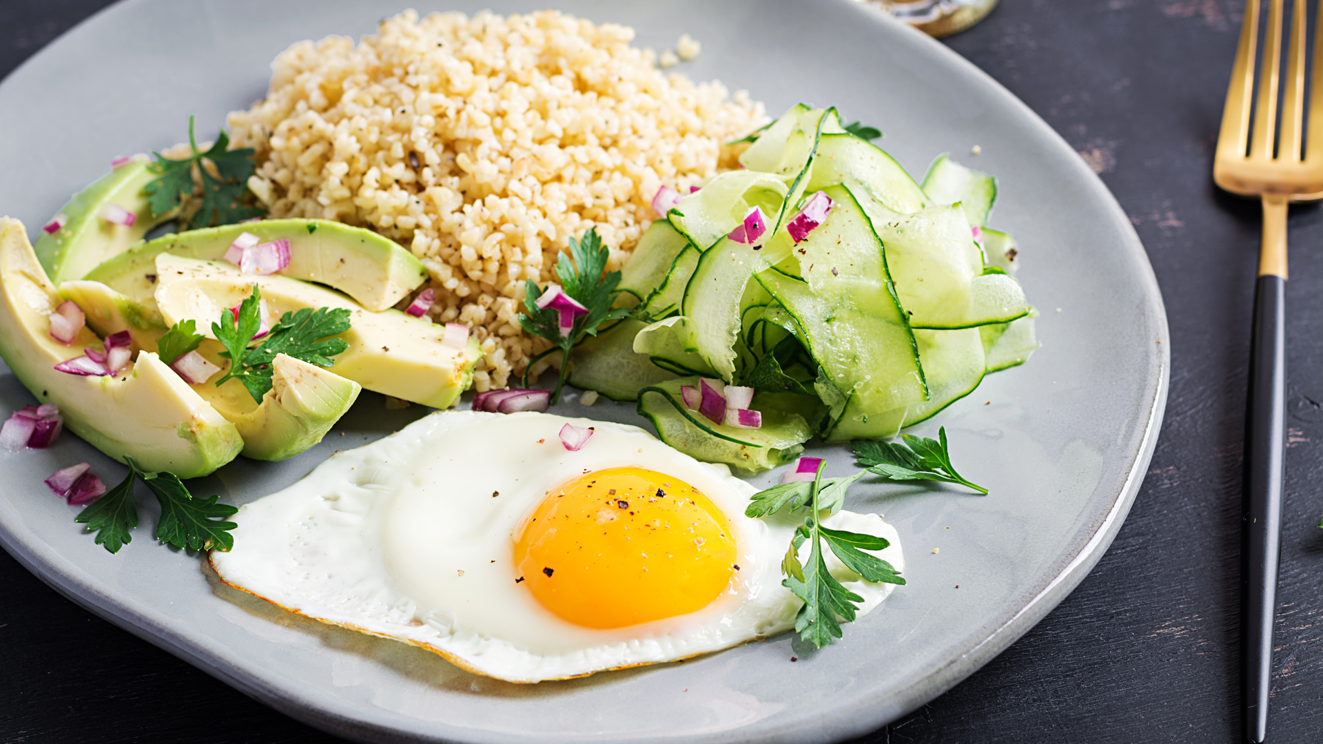 Plate of food: avocado, couscous, cucumber salad, fried egg, garnished with parsley.
