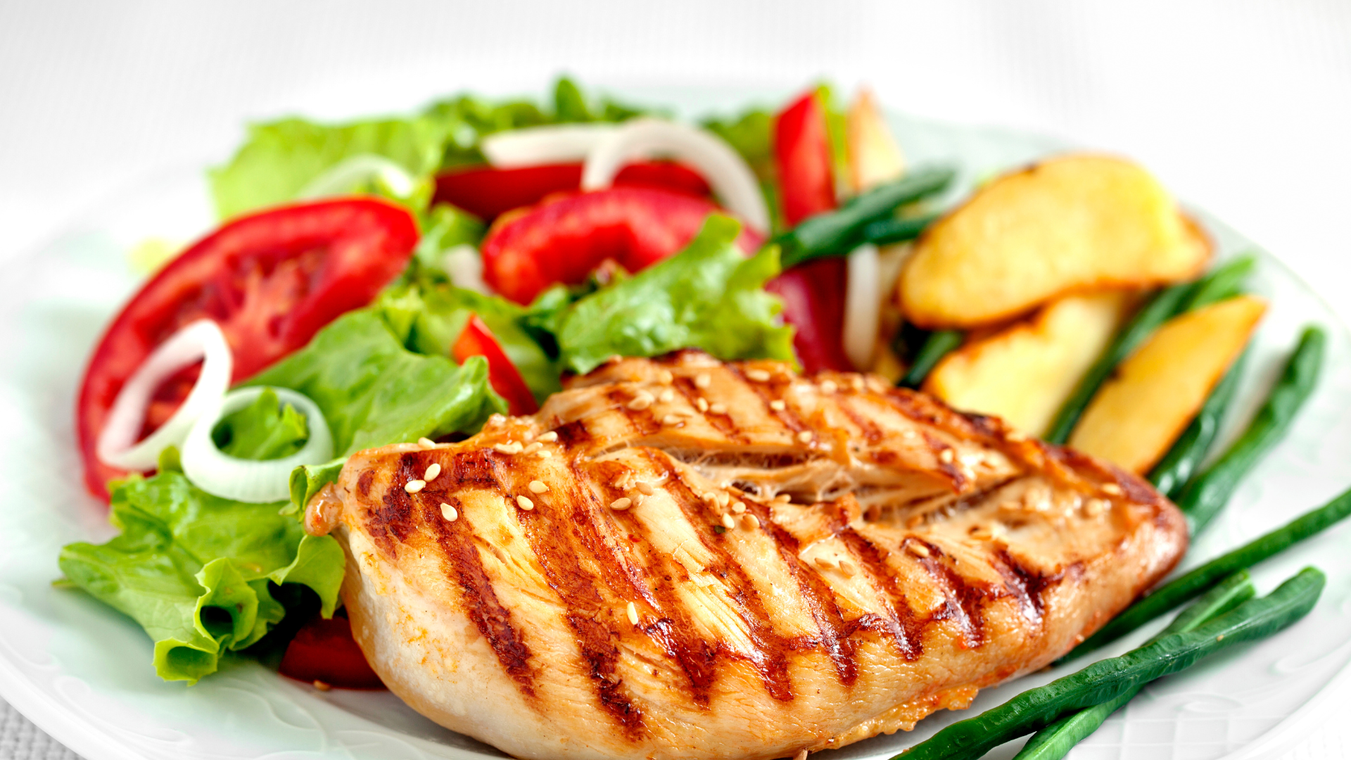 Grilled chicken breast with salad and roasted potatoes on a white plate.