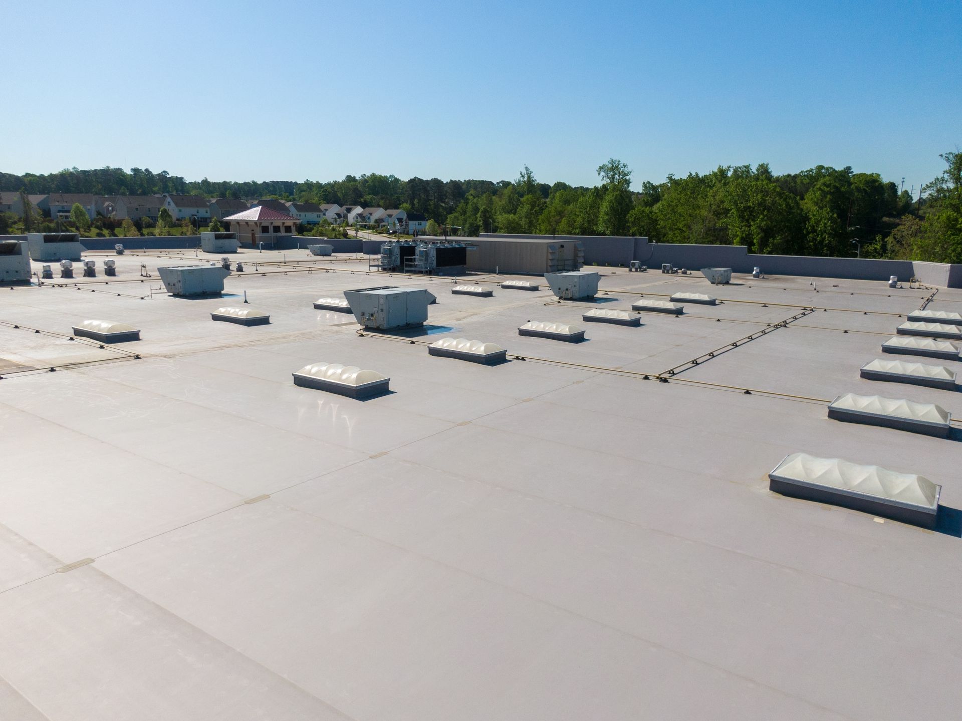 Aerial view of a flat commercial roof with multiple skylights and vents under a clear, blue sky.
