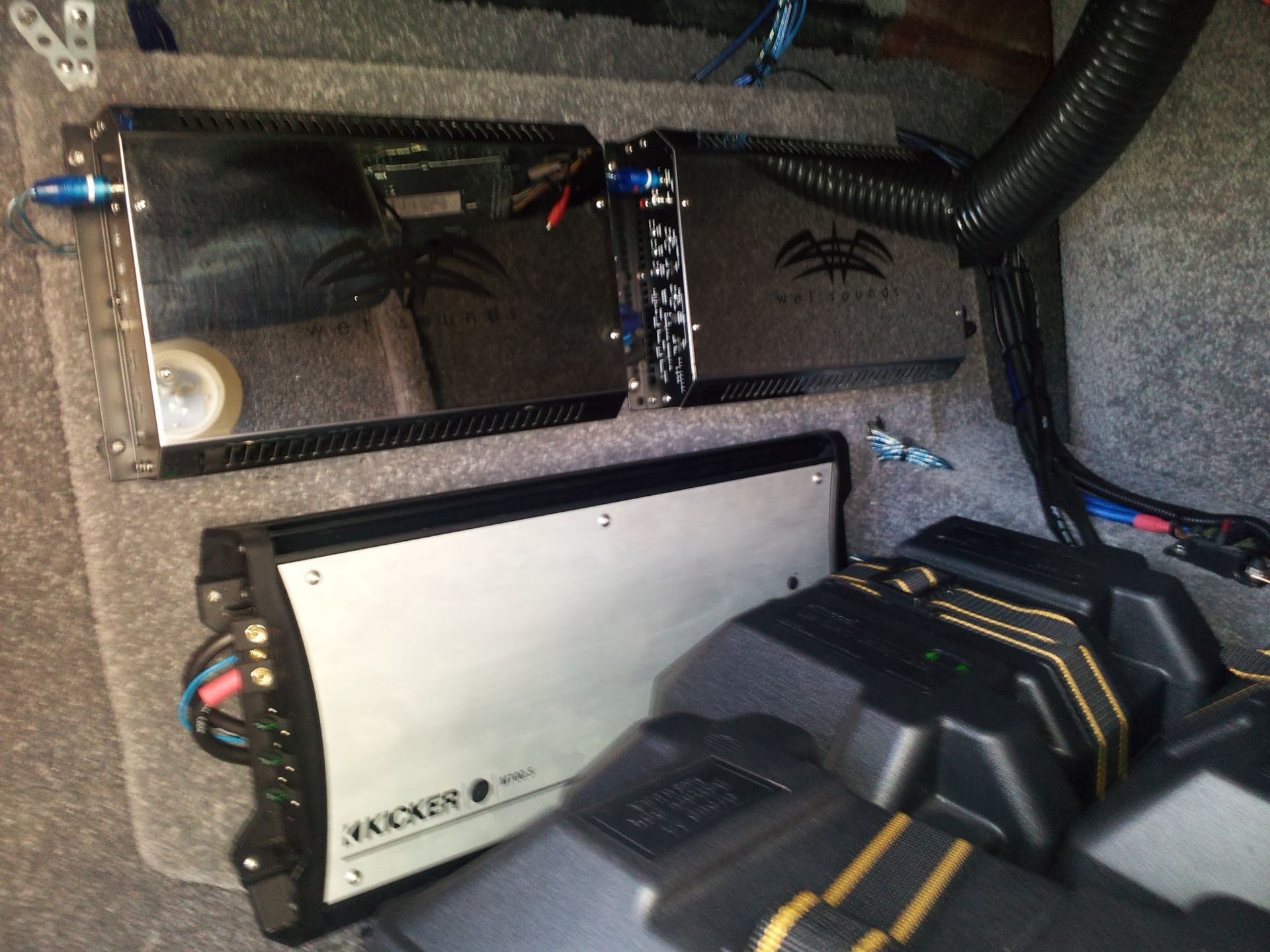 Car audio amplifier and subwoofer installation in a carpeted vehicle trunk, with visible wiring and black components