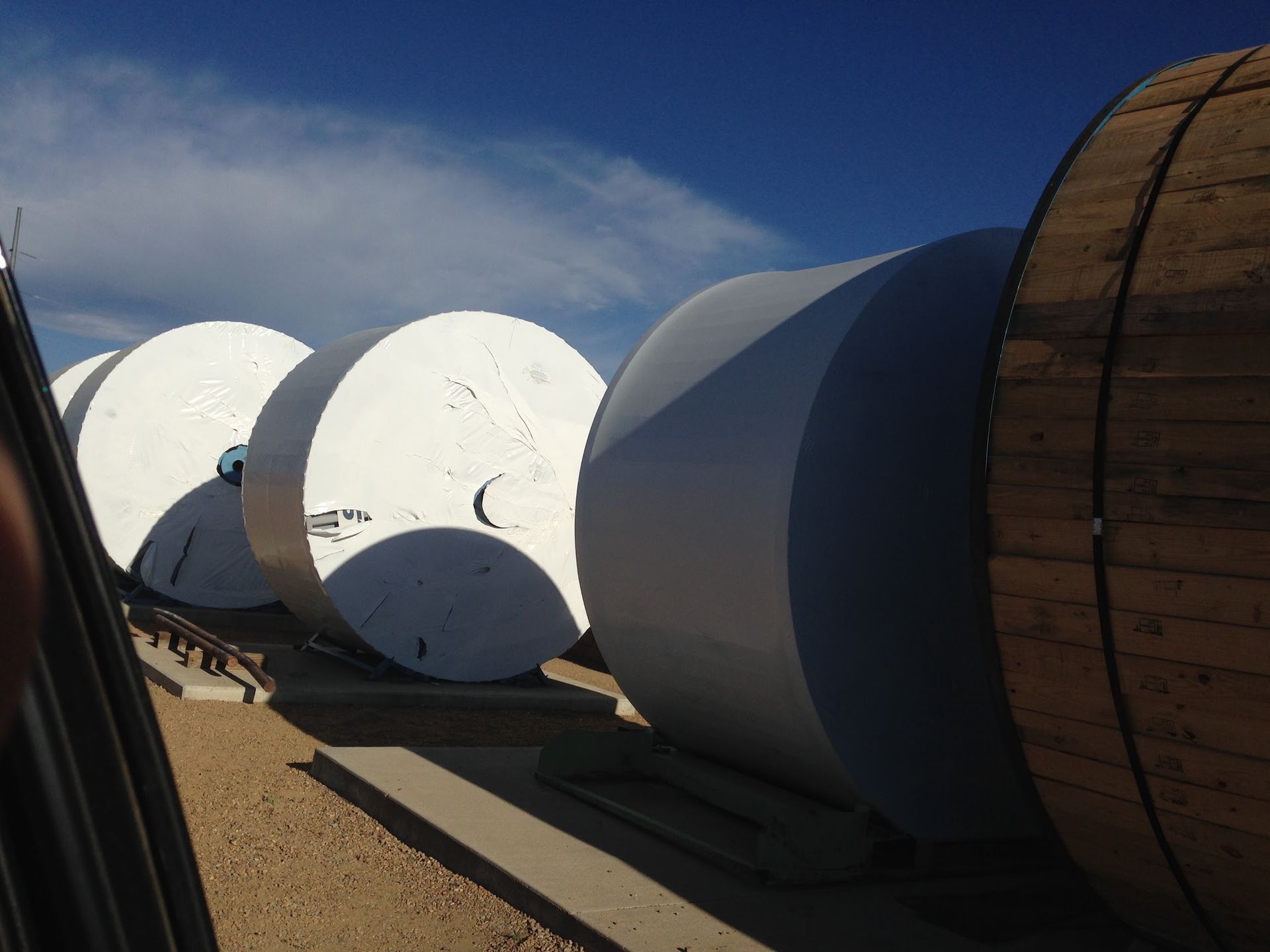 Large white cylindrical tanks or pipes lined up outdoors under a blue sky on a paved surface
