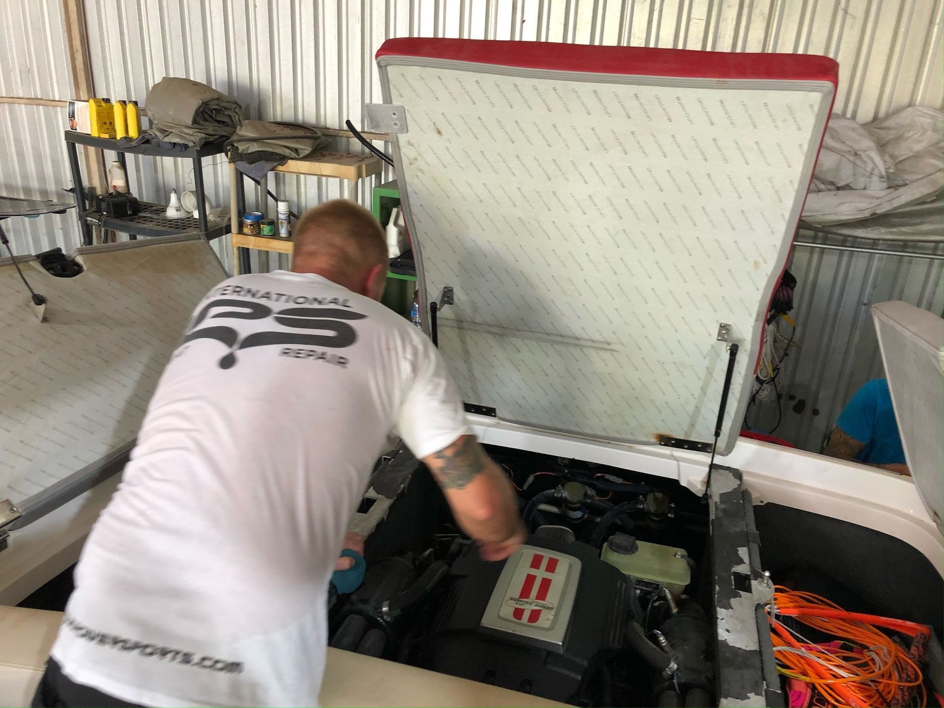 Person inspecting the engine bay of a white car with the hood open in a garage.