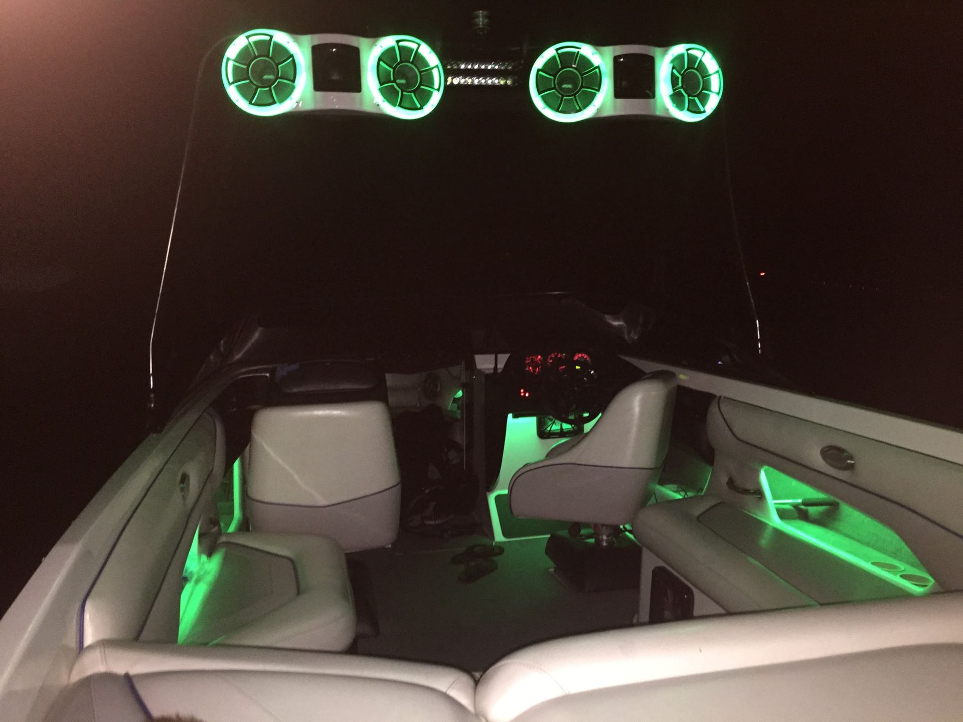 Interior of a boat at night with glowing green speakers and green accent lights on the seats and rails